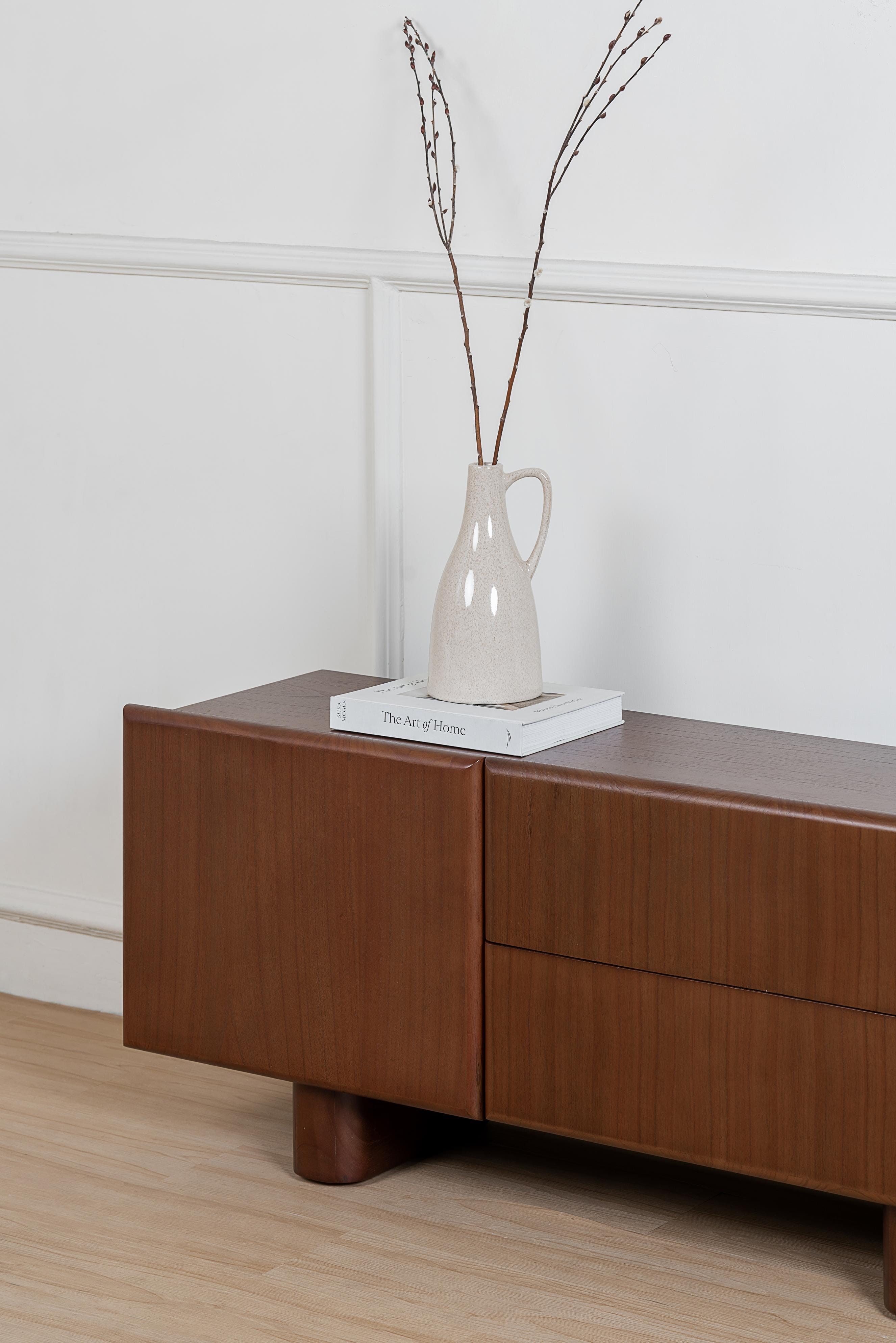 Wooden sideboard with a vase and books on a white wall background