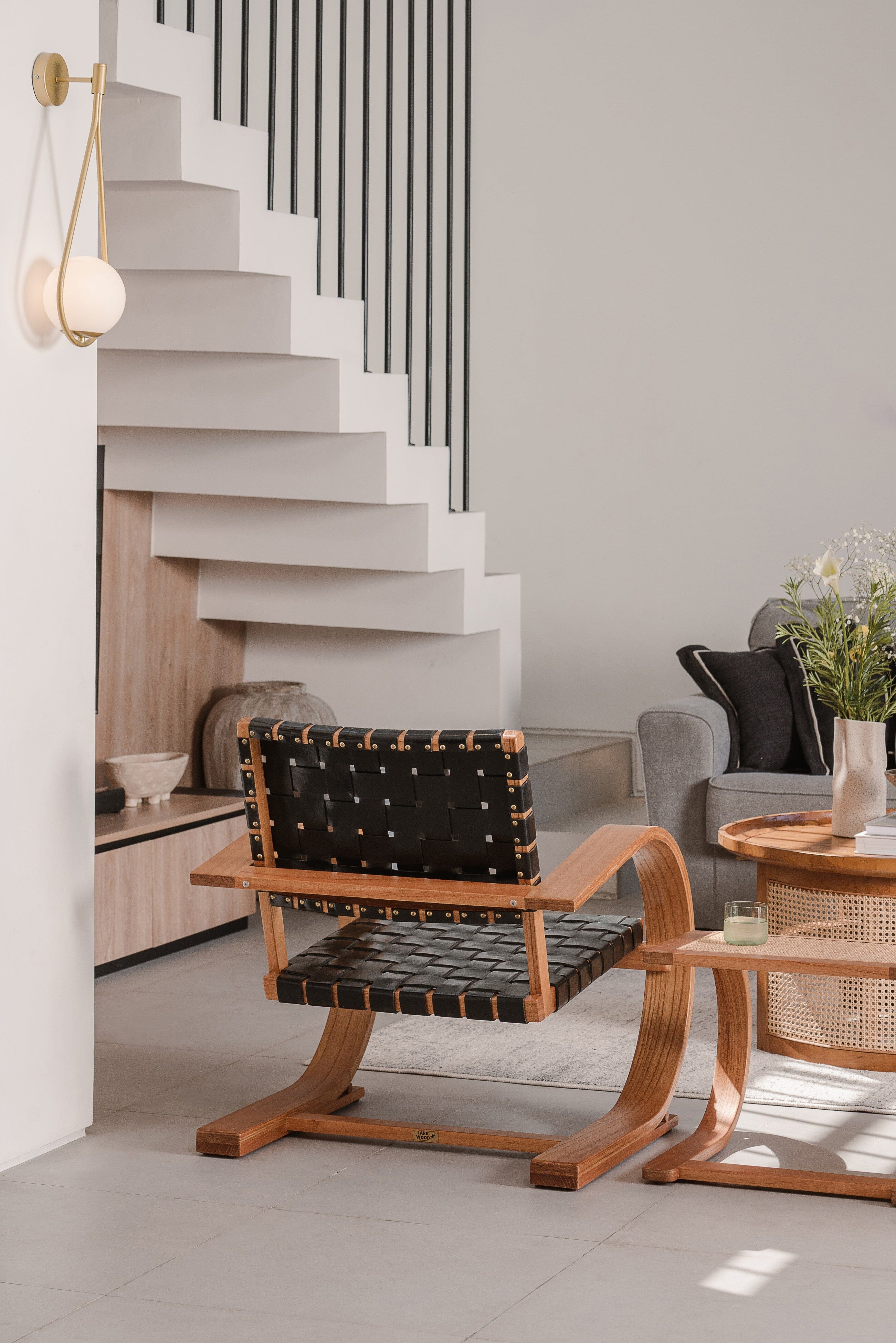 Modern interior with a black and wooden chair, light-colored floor, and staircase.