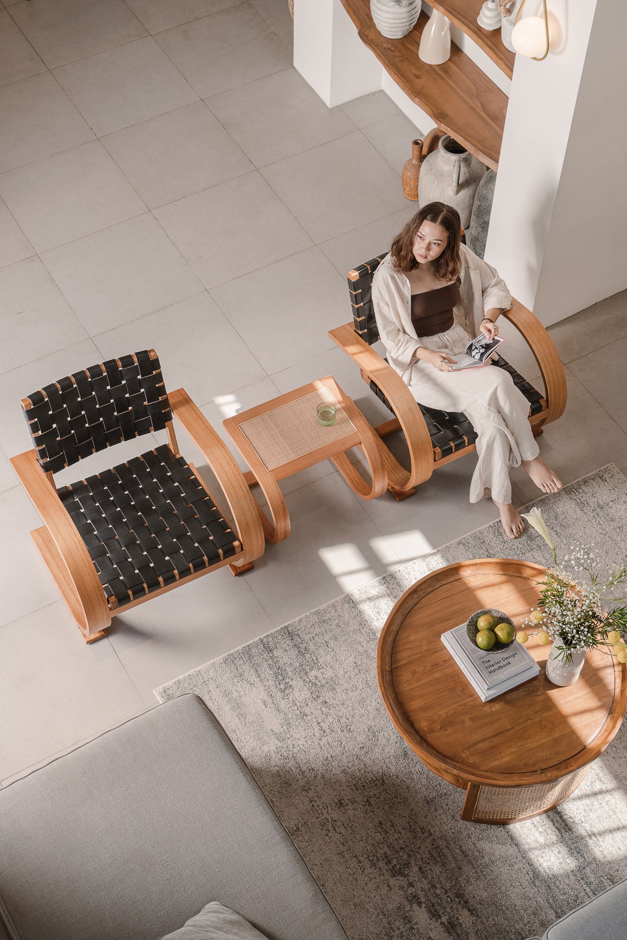 Woman sitting on a wooden chair in a modern living room with a coffee table and decorative items.