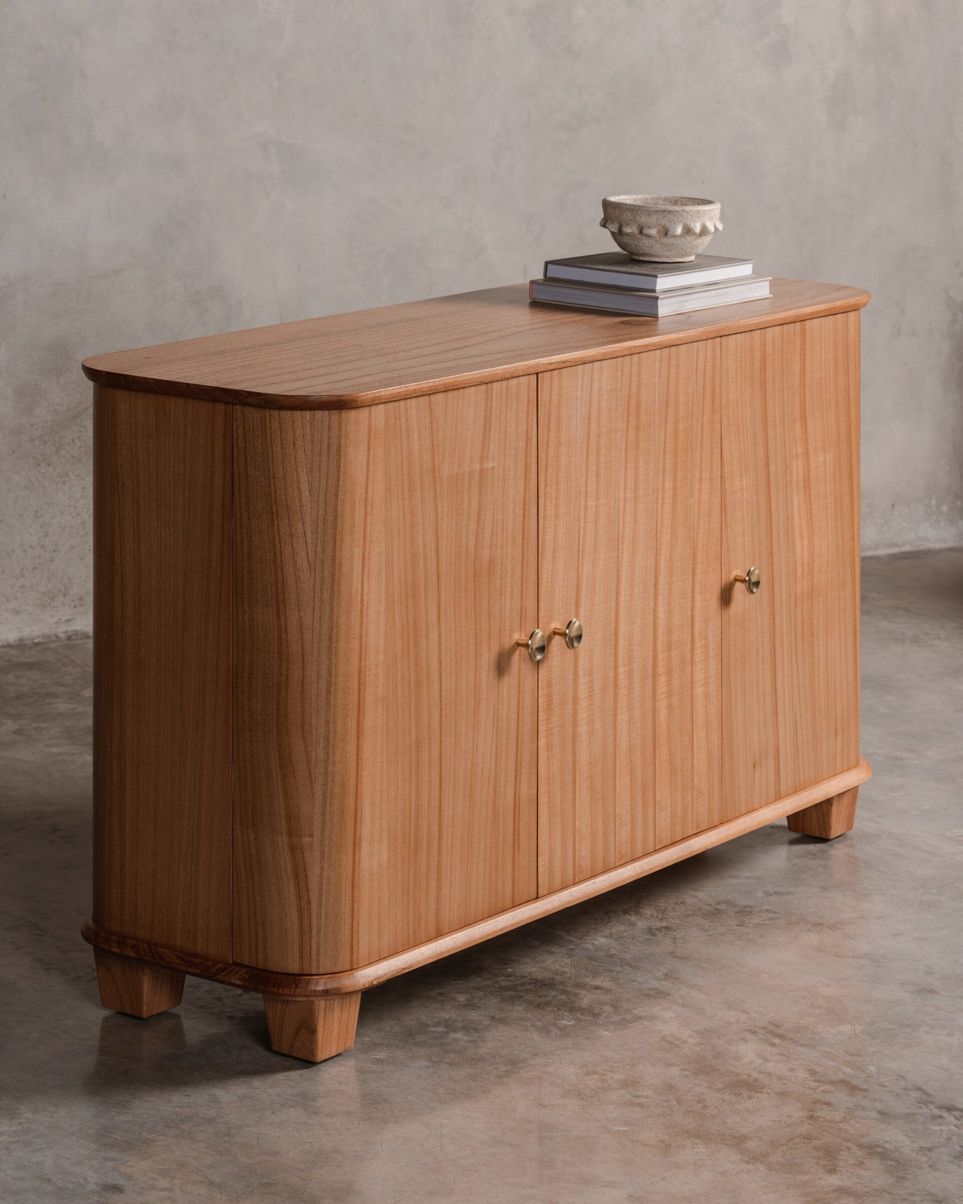 Wooden sideboard console with 3 doors against a grey wall.